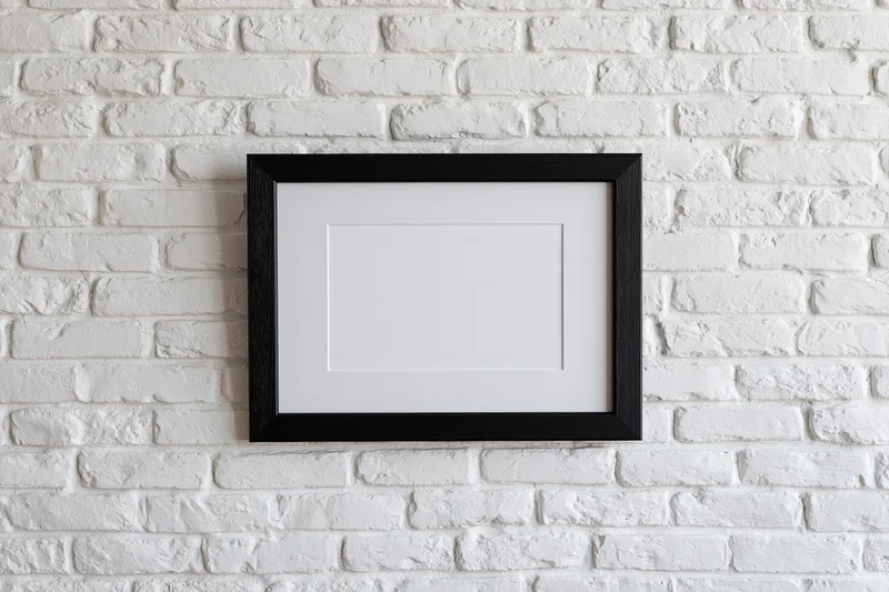 Black wooden picture frame with white mat hanging on white brick wall