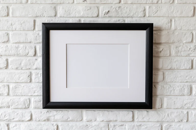 Black wooden picture frame with white mat hanging on white brick wall