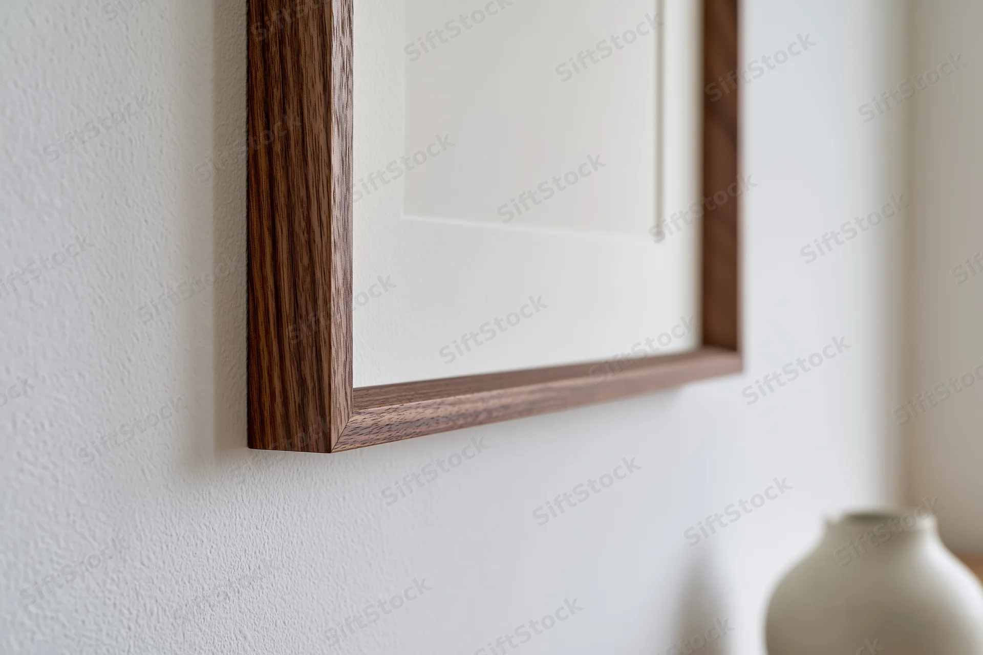 Dark walnut wood picture frame with white mat hanging on a white wall near a ceramic vase