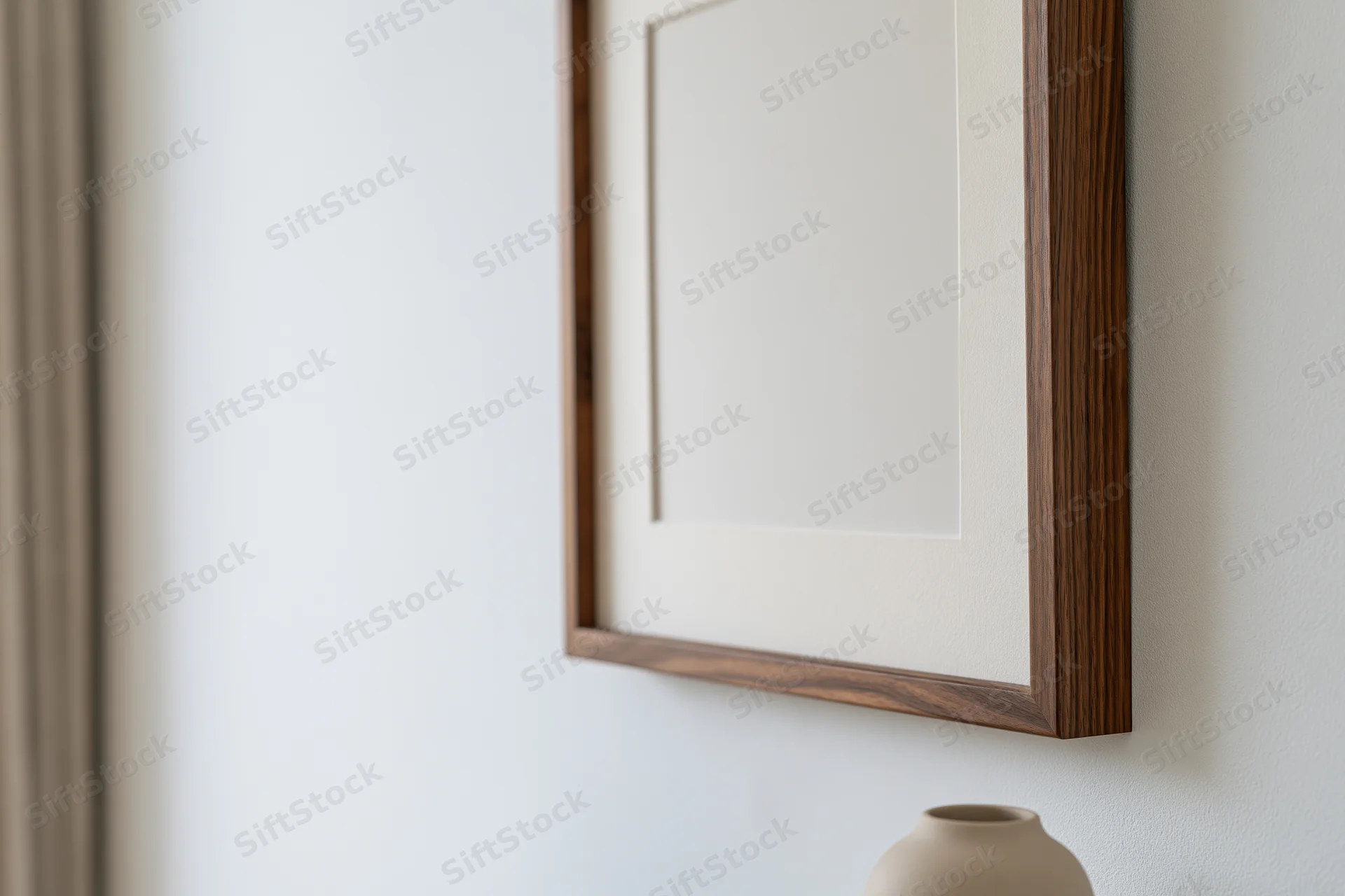 Dark walnut wood picture frame with white mat hanging on a white wall above a small ceramic vase