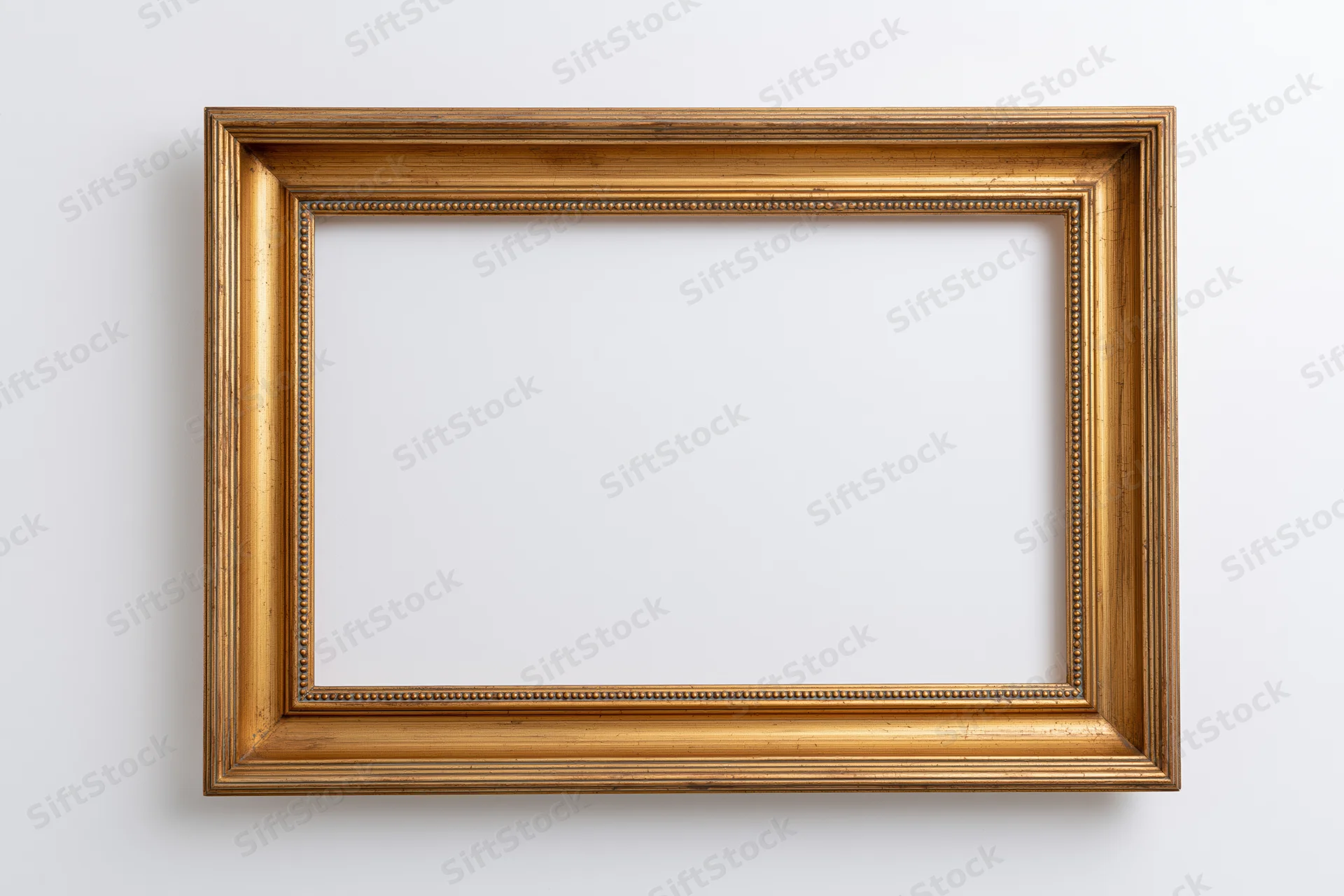 Empty gold ornate picture frame hanging on white wall