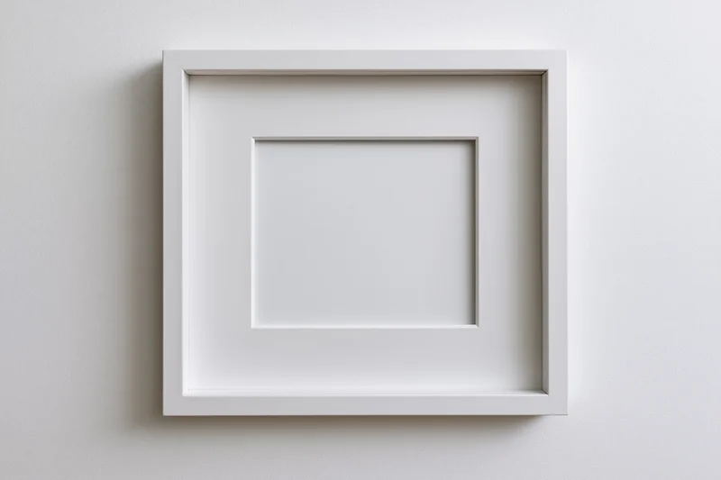 White square picture frame hanging on a plain wall with a mat border and empty center