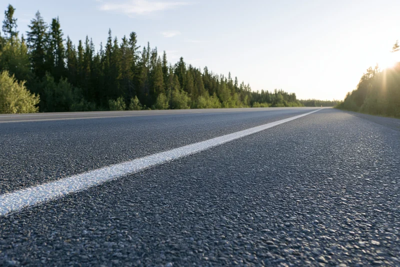 Empty two-lane asphalt highway stretching into the distance lined with evergreen trees under clear sky at sunrise