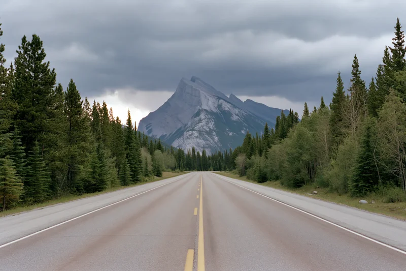 Straight asphalt highway through evergreen forest leading to mountain peak under cloudy sky