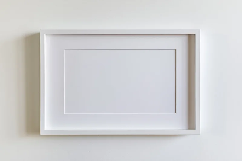 White picture frame with mat border hanging on a plain wall