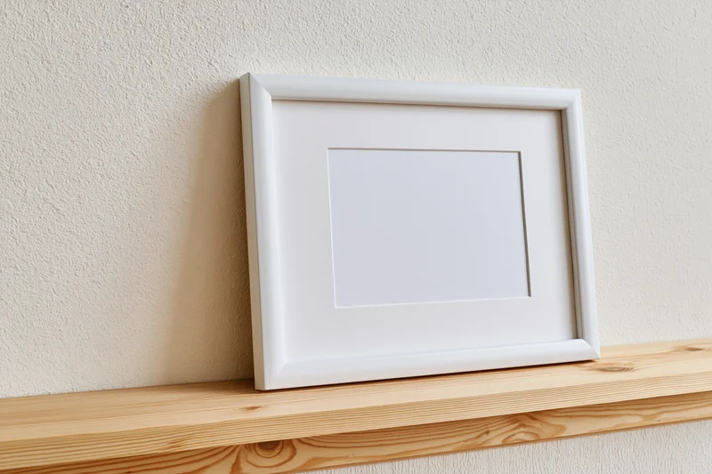 White empty picture frame leaning on wooden shelf against textured wall