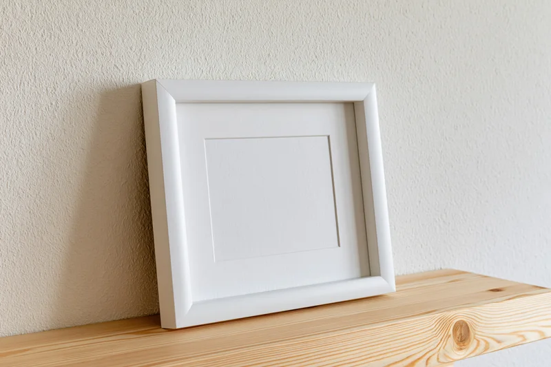 White empty picture frame leaning on wooden shelf against textured wall