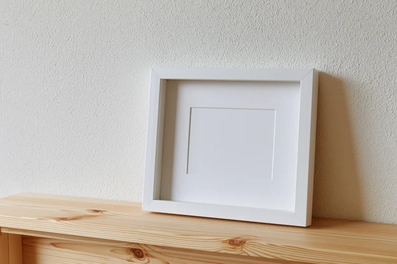 White empty picture frame leaning against textured wall on wooden shelf