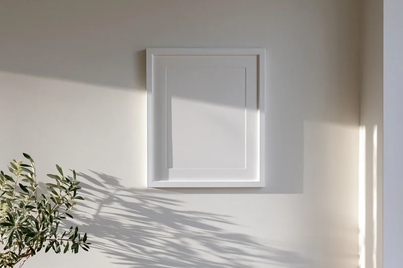 White rectangular frame mounted on a pale wall with plant shadow beside it