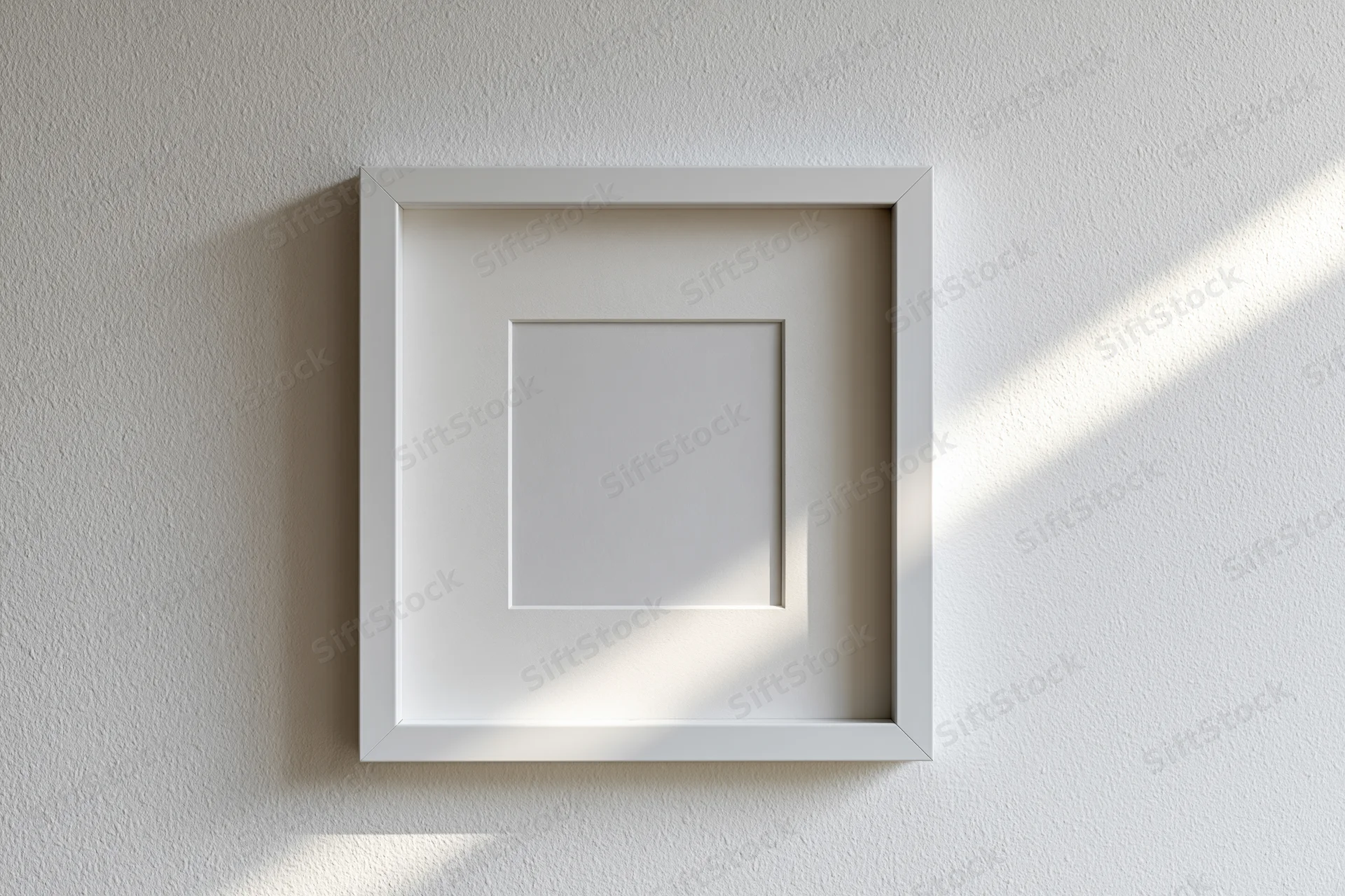 White square picture frame with wide mat hanging on textured wall, sunlight casting diagonal shadow across surface