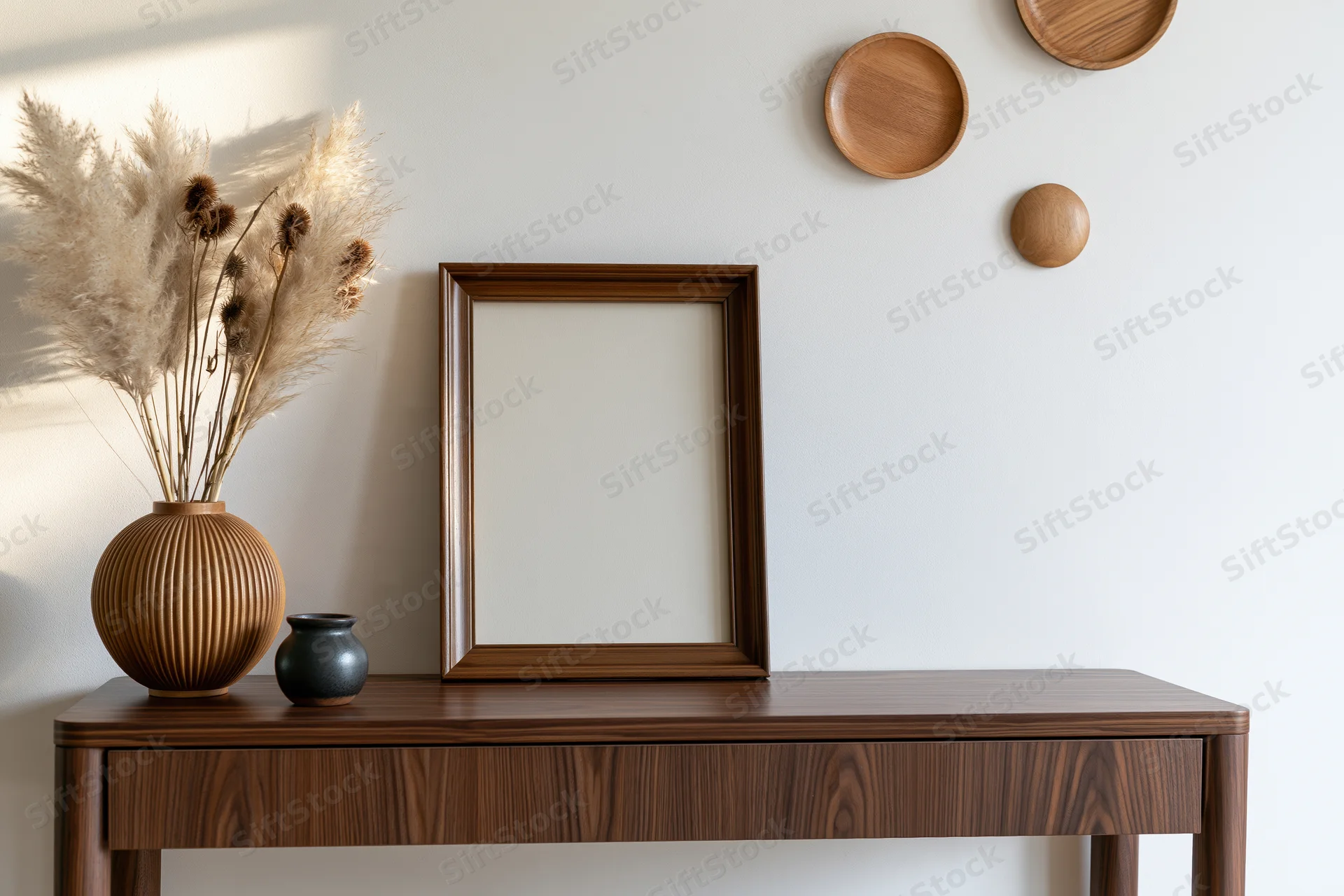 Empty wooden frame leaning on console table with dried pampas grass in vase and wall-mounted wooden plates