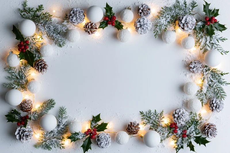 Christmas decoration border with pine, holly, berries, ornaments and lights on white surface