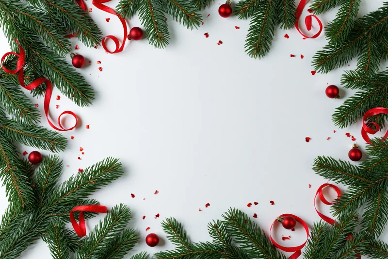 Fir branches and red ribbons arranged as a christmas border frame on white surface with copyspace