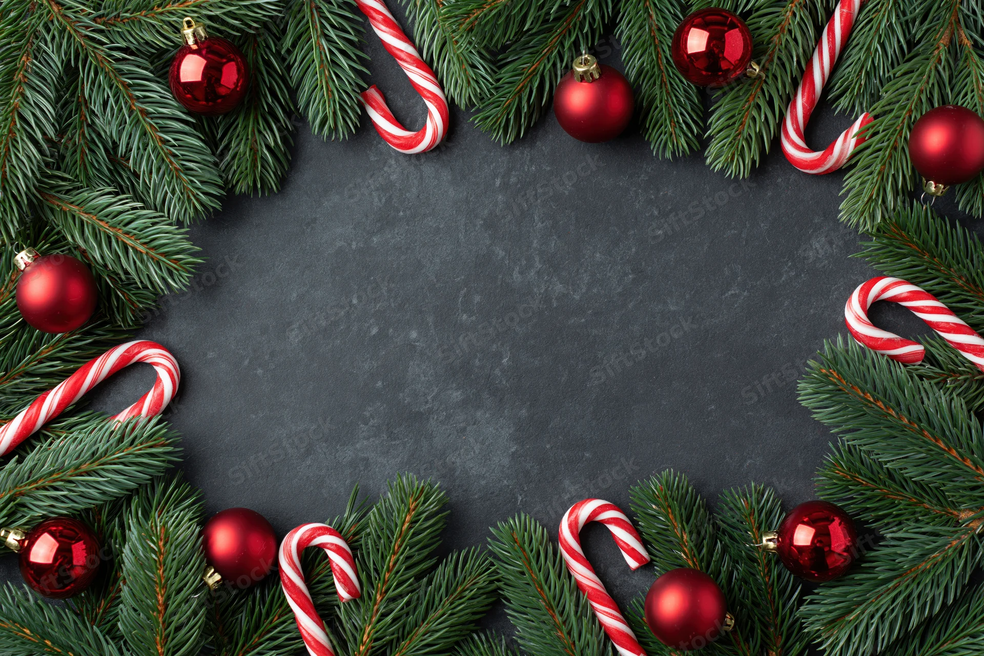 Christmas border frame made of pine branches and red ornaments on dark surface with copyspace