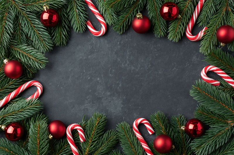 Christmas border frame made of pine branches and red ornaments on dark surface with copyspace