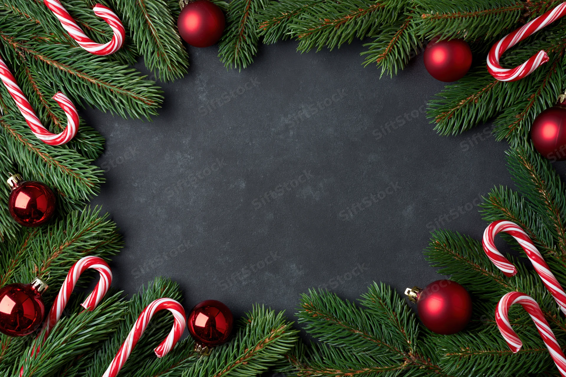 Christmas border frame made of pine branches and red ornaments on dark surface with copyspace