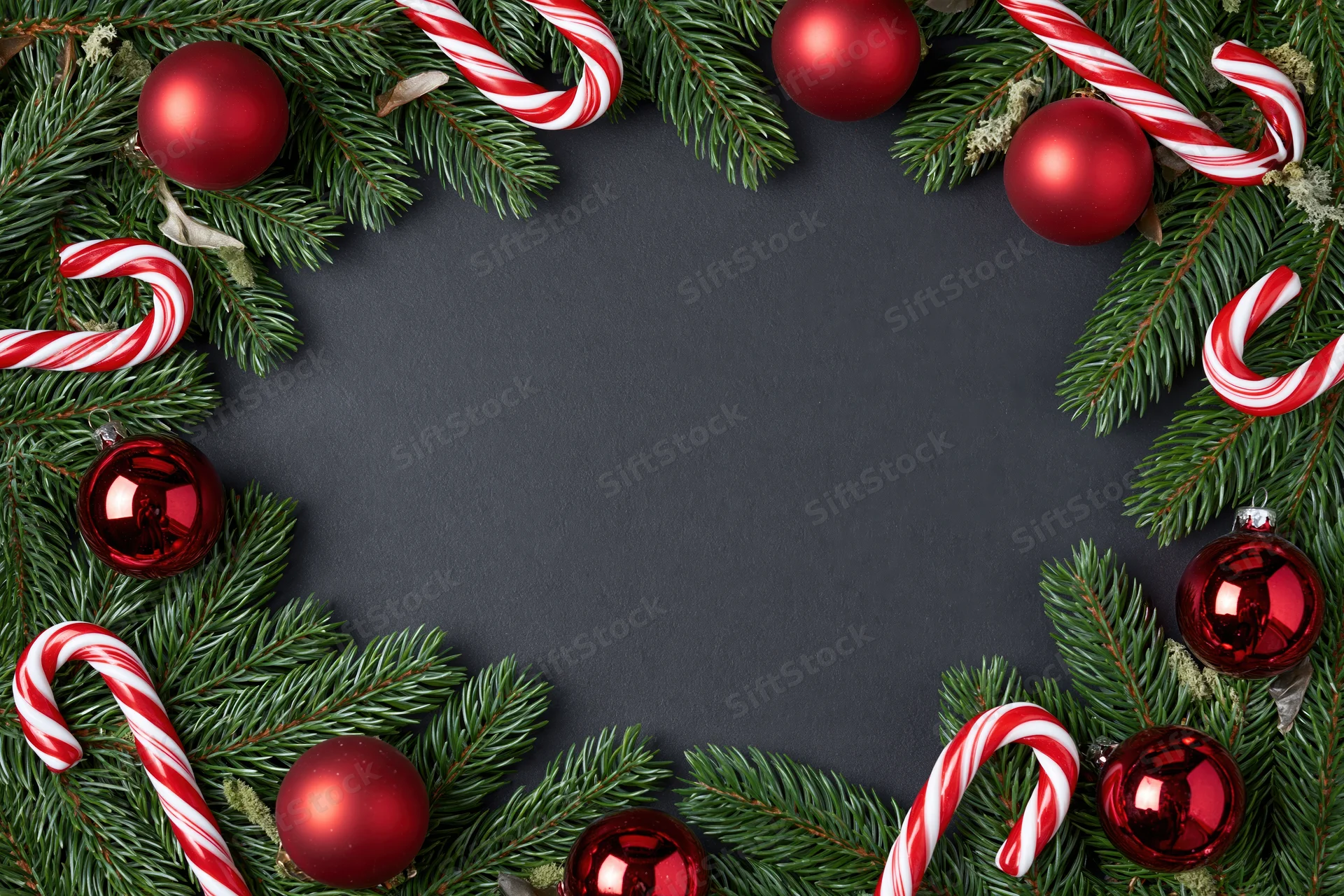 Christmas border frame made of pine branches and red ornaments with candy canes on dark surface