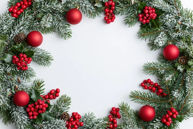 Circular christmas wreath made of frosted pine and fir branches with red berries, holly, ornaments and pinecones forming a border frame on white background
