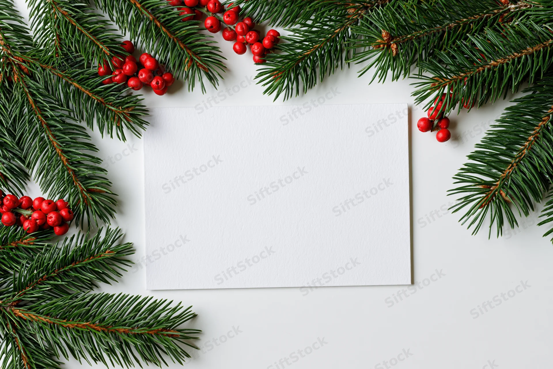 Blank white card surrounded by pine branches and red berries on white surface