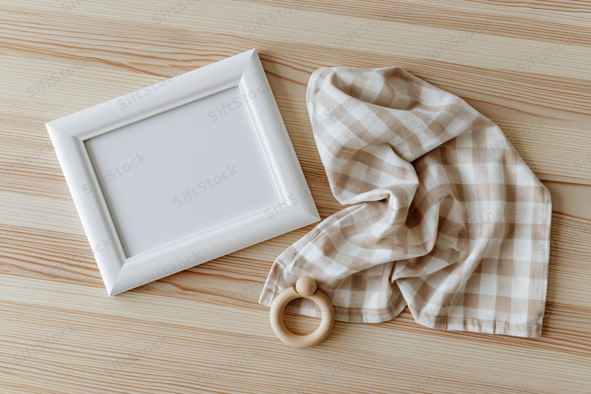 White wooden frame with blank interior and baby teether on checkered cloth on light wood surface