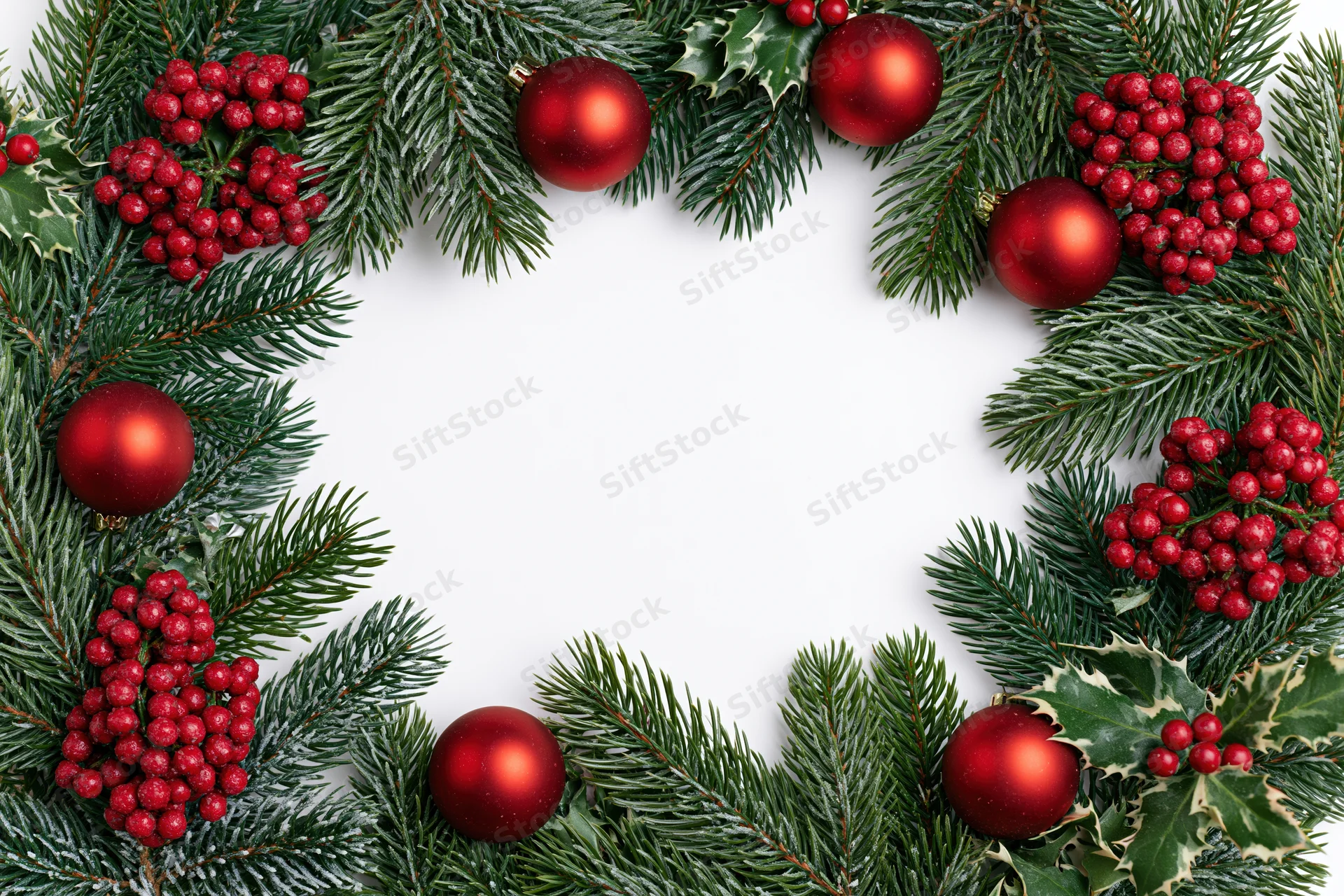 Christmas wreath made of pine branches holly berries and red ornaments arranged in circle on white background with copyspace