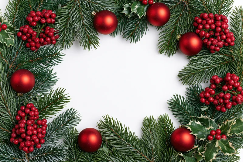 Christmas wreath made of pine branches holly berries and red ornaments arranged in circle on white background with copyspace