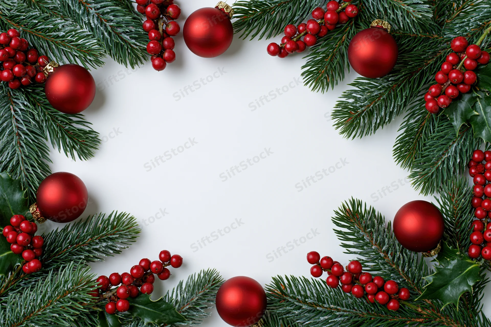 Pine branches and red ornaments arranged in a frame around white copyspace