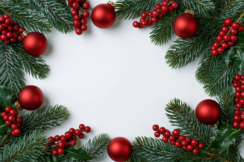 Pine branches and red ornaments arranged in a frame around white copyspace
