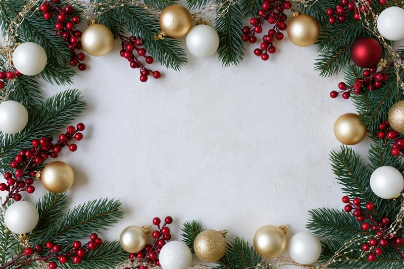 Pine branches and red berries with gold and white ornaments arranged in a frame on a light surface
