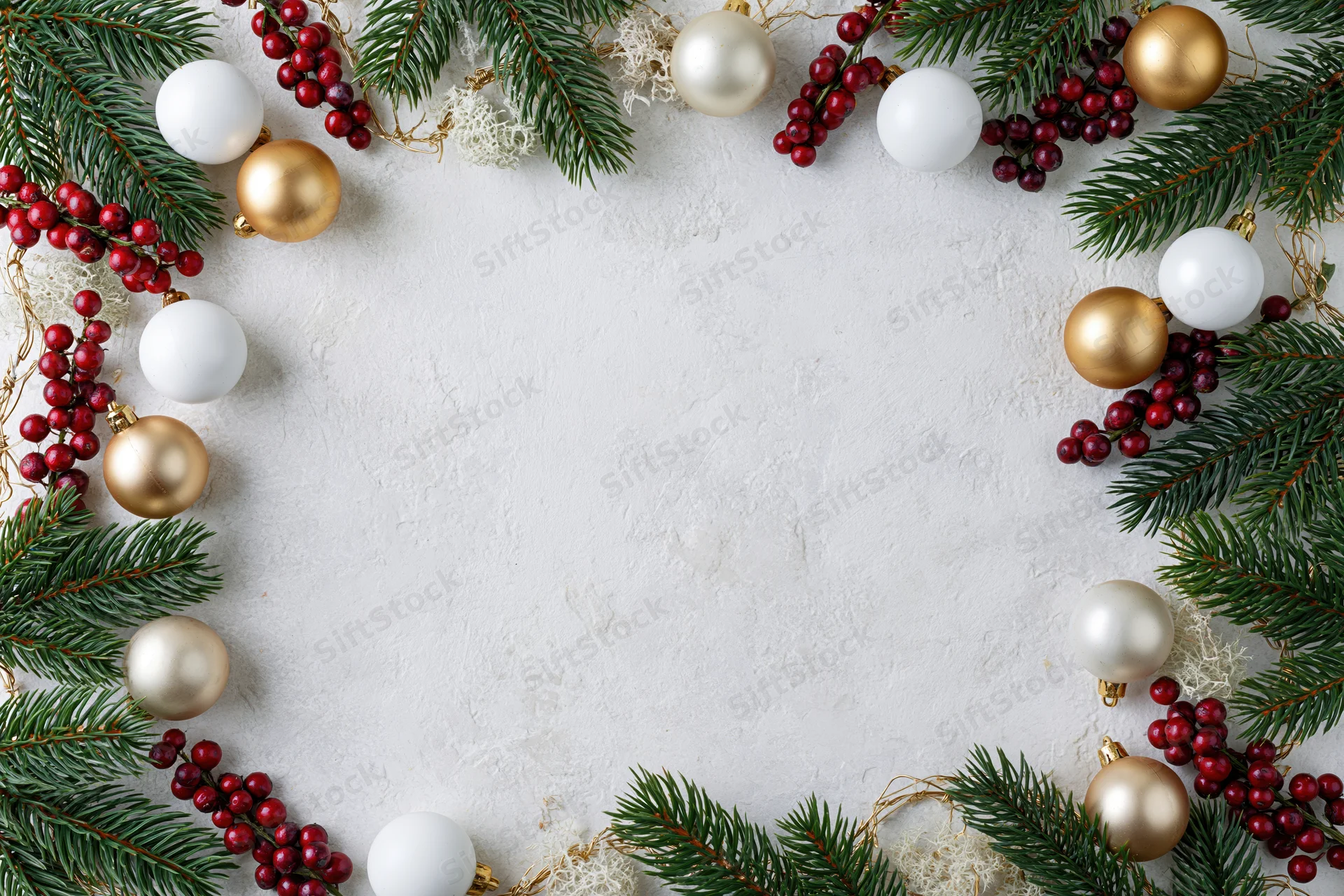 Pine branches and red berries with gold and white ornaments arranged in a frame on a textured white surface