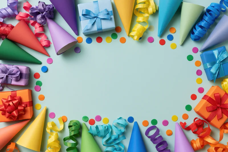 Rainbow party supplies arranged in a frame around a light blue surface with copyspace in the center