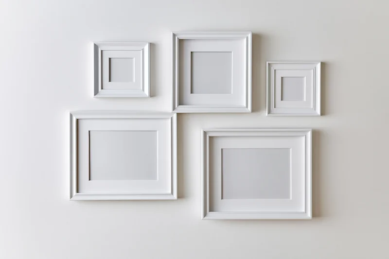 Five empty white picture frames arranged asymmetrically on a plain wall