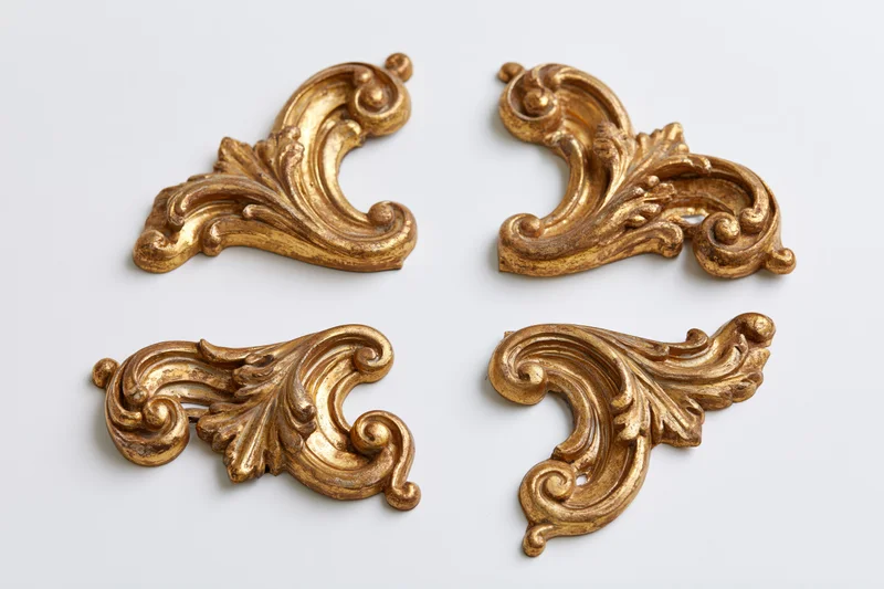 Four ornate gilded baroque corner ornaments arranged symmetrically on white background