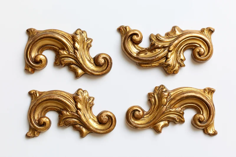 Four ornate gilded baroque corner pieces arranged symmetrically on white background