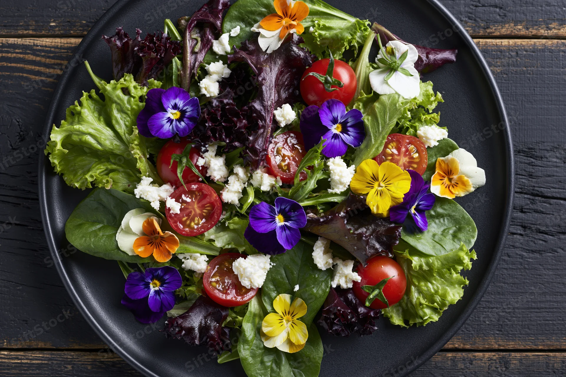 Fresh garden salad with mixed greens, cherry tomatoes and edible flowers on a dark plate over rustic wood