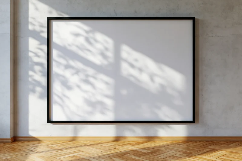 Black-framed empty canvas hanging on concrete wall with leaf shadows in minimalist interior