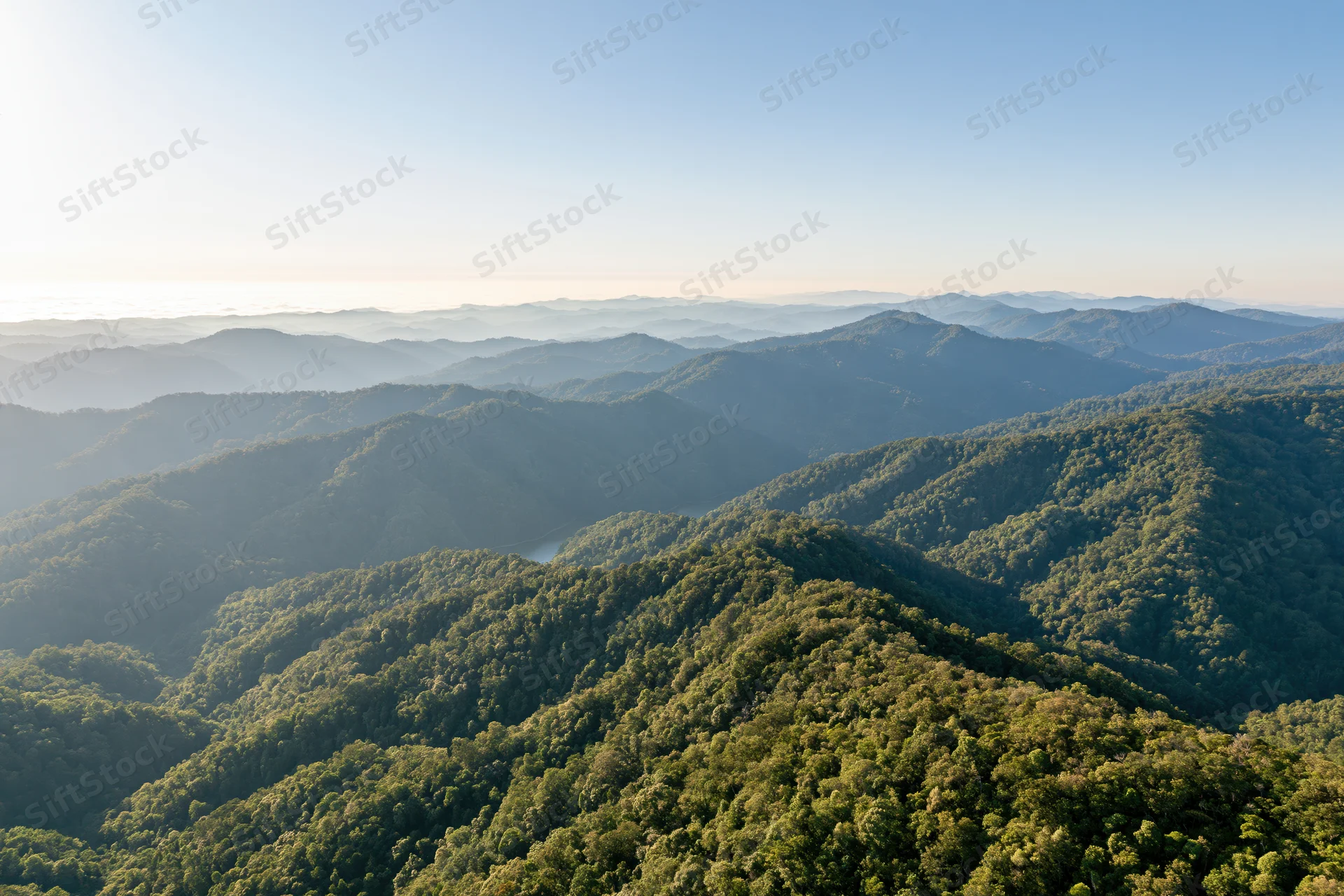 Aerial view of layered green mountain ridges stretching to the horizon under clear sky