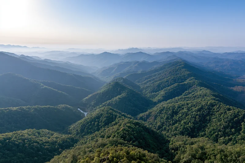 Aerial view of layered green mountain ridges stretching to the horizon under clear blue sky
