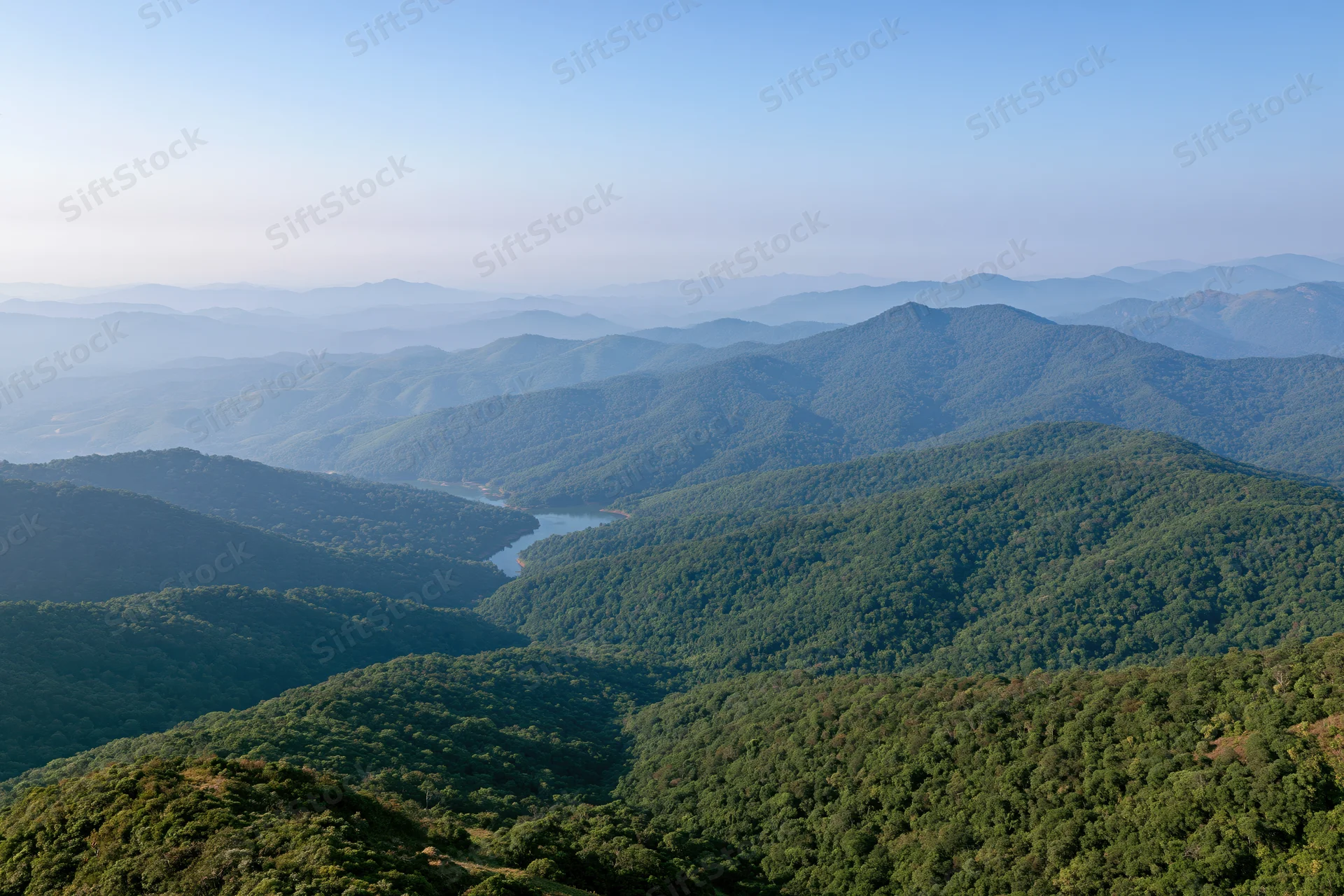 Aerial view of layered green mountain ridges stretching to the horizon with forested valleys and hazy sky