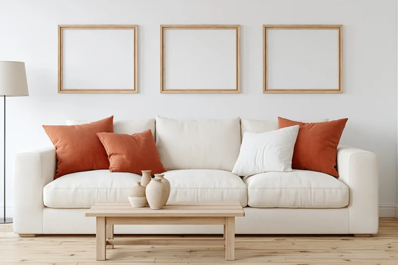 Cream linen sofa with orange and white cushions in a minimalist scandinavian living room with wooden coffee table and framed wall art