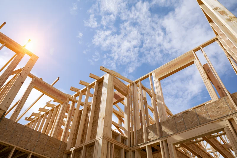 Wooden frame of a new house under construction against a blue sky with sun and clouds