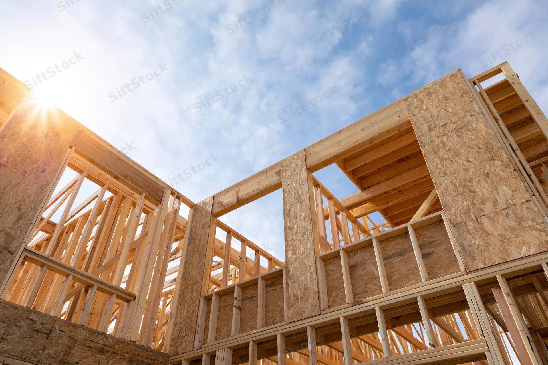 Wooden frame of a new residential house under construction against a blue sky with sun flare