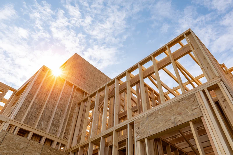 Wooden frame of a new residential house under construction against a blue sky with sun shining through the beams