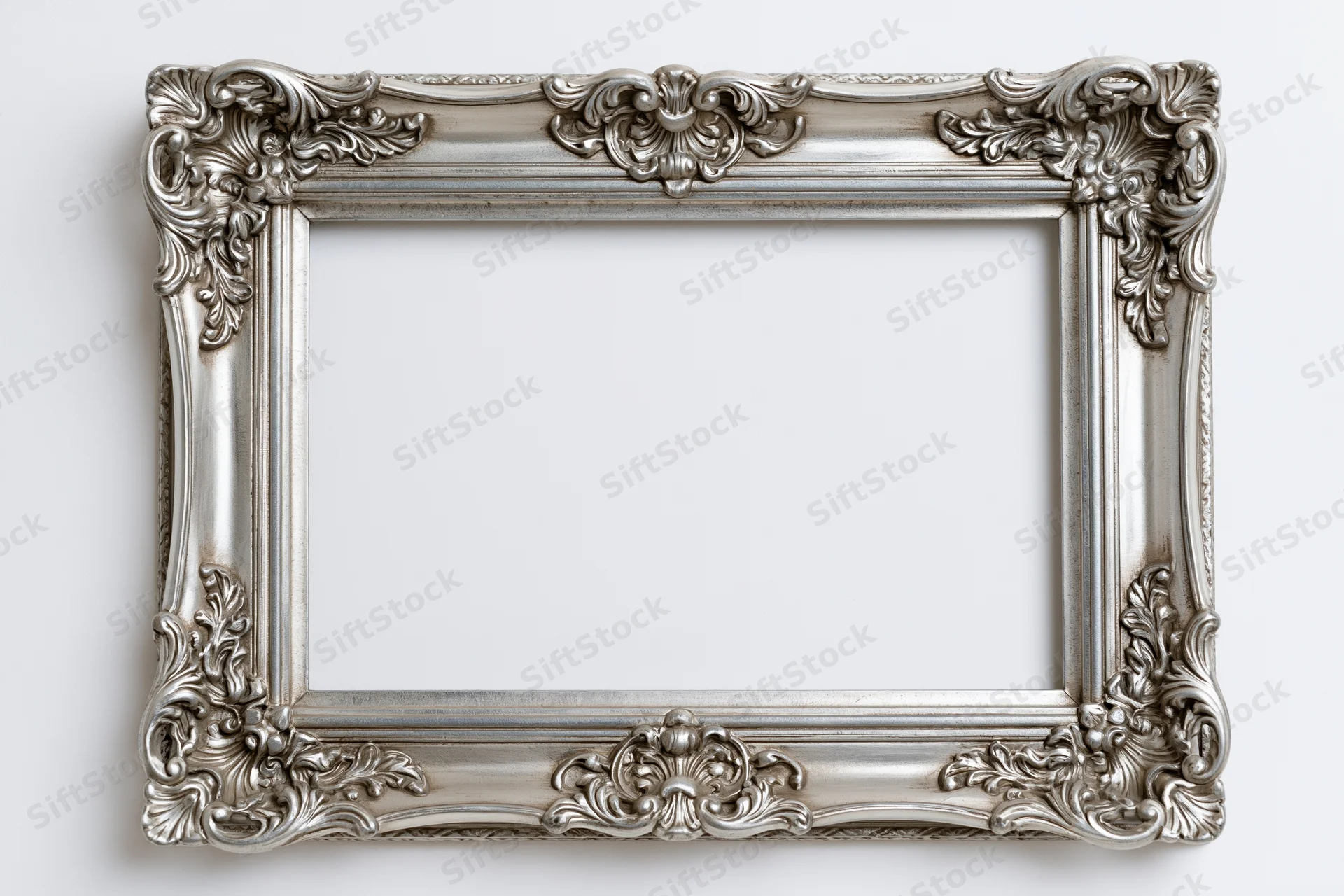 Ornate silver picture frame with baroque floral details hanging on a white wall