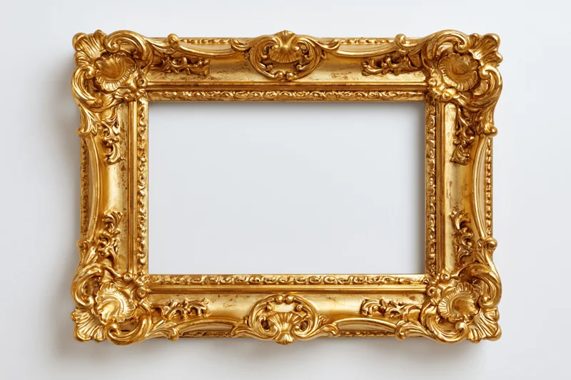 Ornate baroque gold picture frame with intricate carved scrollwork hanging on a white wall