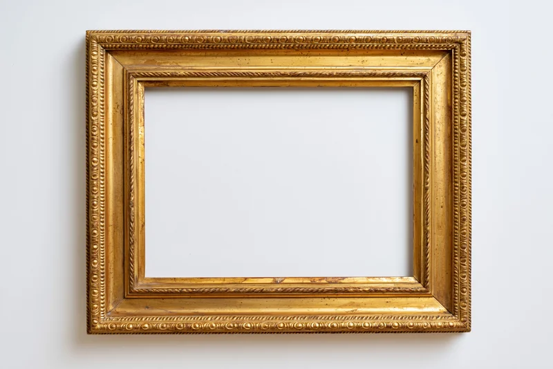 Ornate gilded wooden picture frame hanging on a white wall with empty center
