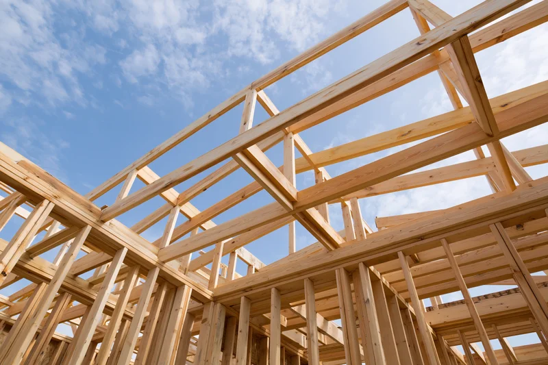 Wooden framing structure of a residential house under construction against a blue sky