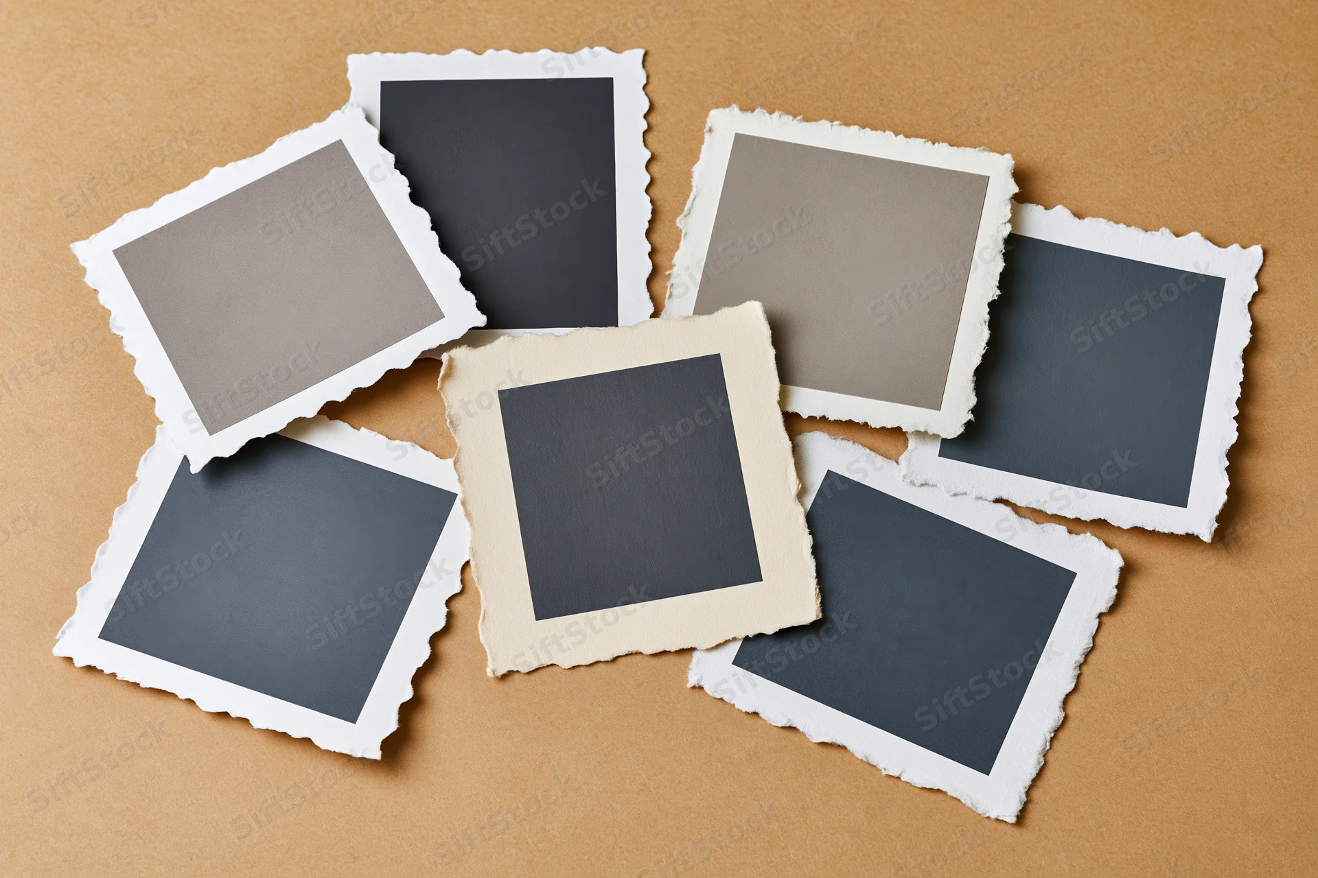 Seven blank vintage photo prints with deckle edges arranged on a brown textured surface