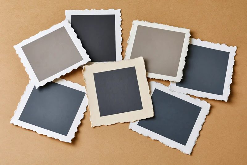Seven blank vintage photo prints with deckle edges arranged on a brown textured surface