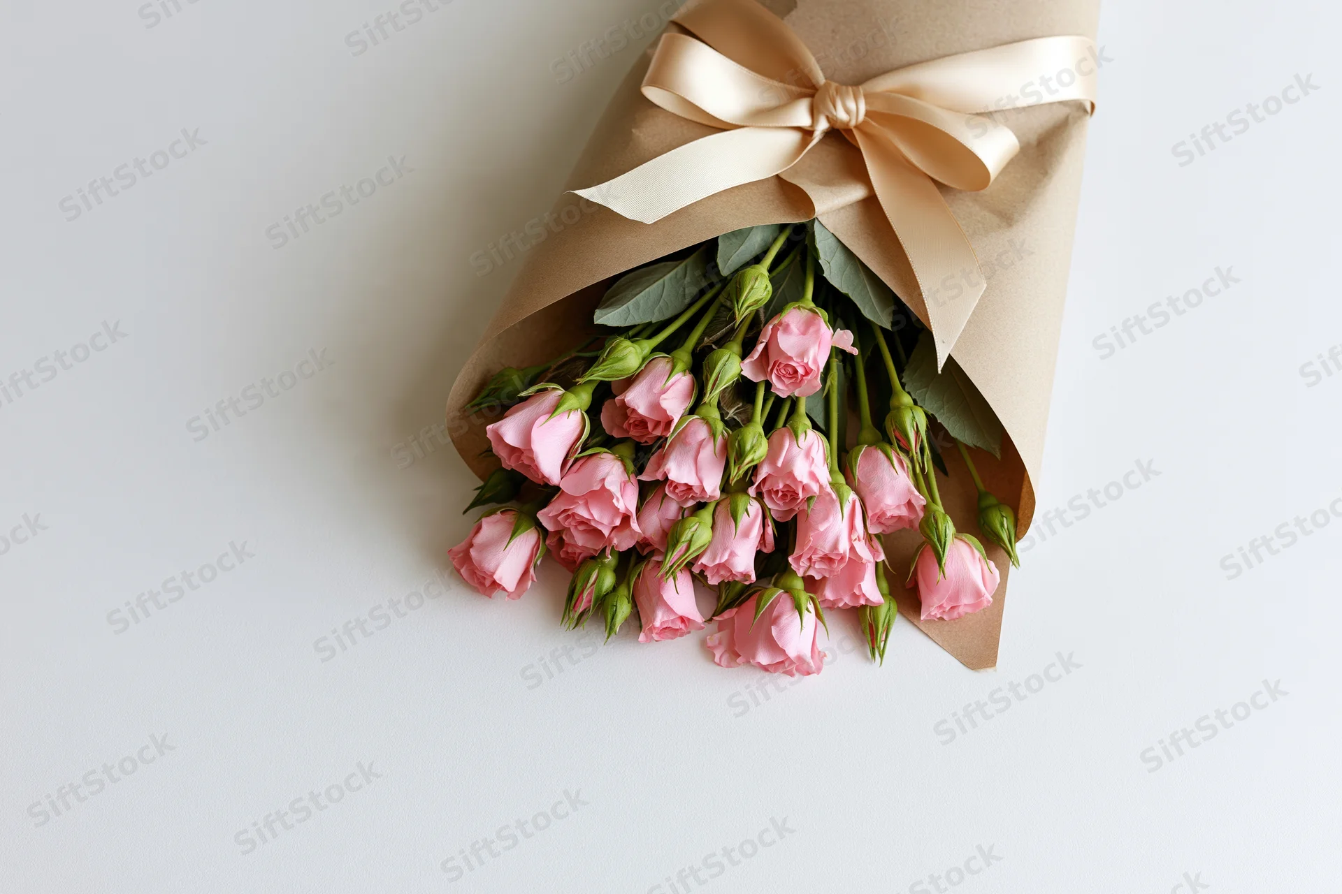Small bouquet of pink spray roses wrapped in kraft paper with beige ribbon on white surface